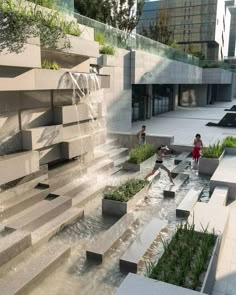 two children playing in the water at an outdoor fountain with steps and planters on either side