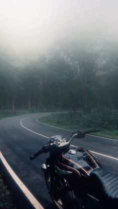 the motorcycle is parked on the side of the road in the foggy forest area