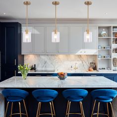 a kitchen with marble counter tops and blue stools in front of an island that has gold barstools