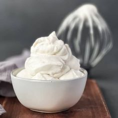 a white bowl filled with whipped cream next to a whisk on top of a wooden cutting board