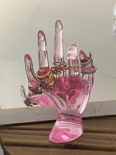 a pink glass hand with lots of rings on it sitting on a wooden table in front of a mirror