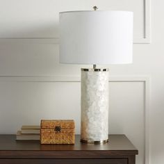 a white lamp sitting on top of a wooden table next to a basket and book