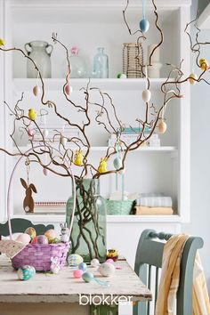 an easter tree in a vase with eggs on the table and other decorations around it