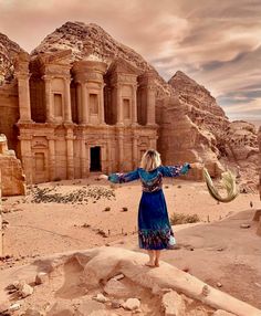 a woman standing on top of a rock formation in front of a desert like area