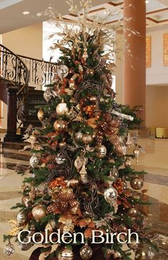 a christmas tree with gold and silver ornaments in the middle of a large lobby area