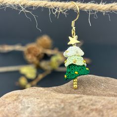 a small christmas tree is hanging from a gold earring on a rock with some branches in the background