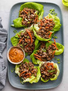 lettuce wraps with ground beef and carrots on a blue plate next to dipping sauce