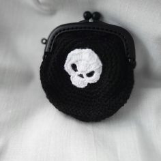 a crocheted skull coin purse on a white cloth with a black chain around it