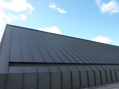 a metal roof on top of a building under a blue sky with clouds in the background