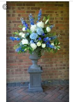 a vase with blue and white flowers in it on a brick floor next to a wall