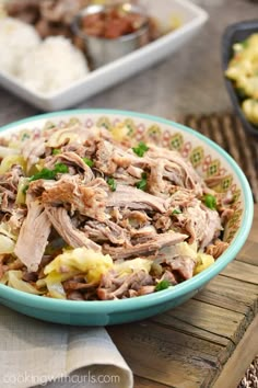 a blue bowl filled with meat and vegetables on top of a wooden table next to other dishes