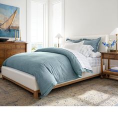 a bed with blue and white comforters in a bedroom next to a painting on the wall