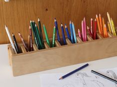 pencils are lined up in a wooden holder on a table next to a drawing