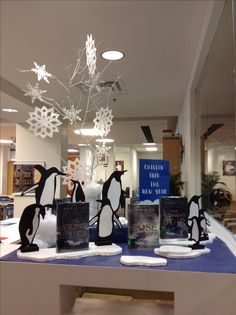 penguins are on display in the window of a book store with snowflakes hanging from the ceiling