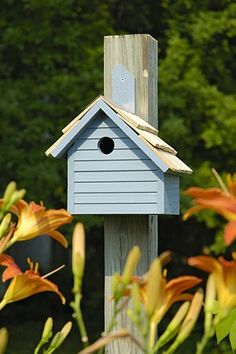 a blue birdhouse sitting on top of a wooden post in front of some flowers