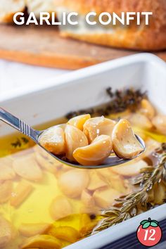 a spoon full of garlic confit in a white dish with herbs on top