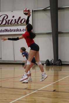 two girls playing volleyball in a gym with one reaching up to hit the ball while another tries to block it