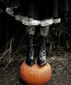 a woman in black boots standing on top of an orange pumpkin with her legs crossed