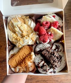 a box filled with assorted desserts on top of a wooden table next to a person's hand