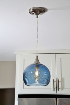 a blue glass light hanging from the ceiling above a refrigerator in a kitchen with white cabinets