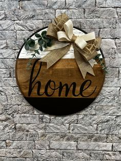 a wooden sign that says home with a bow on it and greenery in front of a brick wall