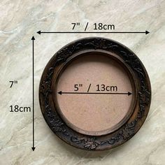 the measurements for a round wooden frame on a marble surface with an arrow pointing up to it