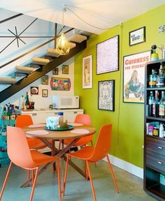 a dining room table with orange chairs and an open bookcase in the corner next to it