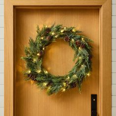 a christmas wreath on a door with lights and pine cones hanging from the front frame