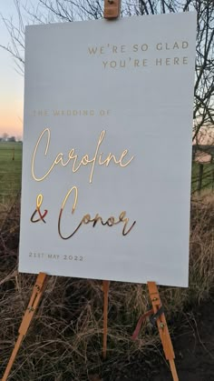 a white sign with gold writing on it sitting in the middle of a grass covered field