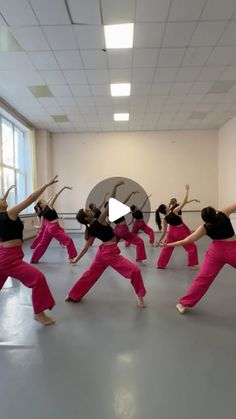 a group of women in pink pants are doing dance moves with their arms up and legs spread out