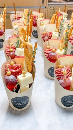 several cups filled with different types of food on top of a white table covered in paper