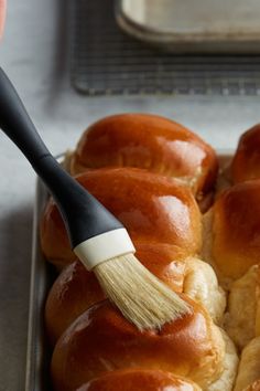 a person holding a brush over some bread rolls