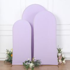 two purple arches with flowers and greenery in front of them on a wooden floor