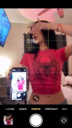 a woman in a red shirt is holding a cell phone and taking a selfie