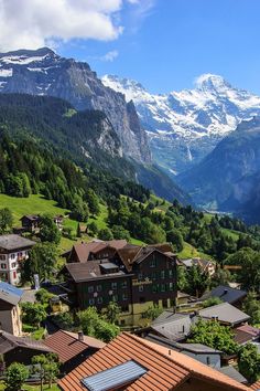 the mountains are covered in snow and green grass, while houses stand on either side