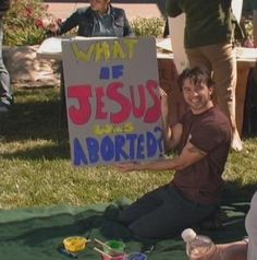 a man sitting on the ground holding a sign that says what if jesus adopted?