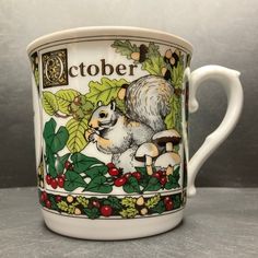 a coffee cup with an image of a squirrel and holly leaves on the bottom is sitting on a table