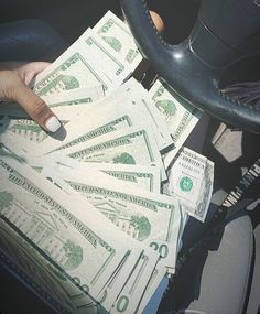 a person driving a car with lots of money in their hand and the steering wheel