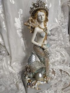 a mermaid figurine sitting on top of a white lace covered tablecloth next to a curtain