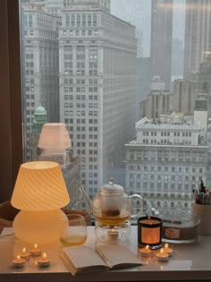 a table with candles, books and a teapot on it in front of a window