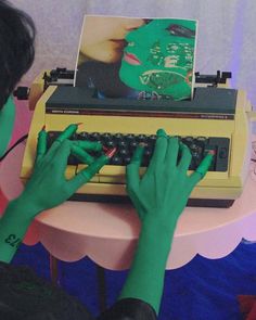 a person typing on an old fashioned typewriter with green painted hands and fingers,