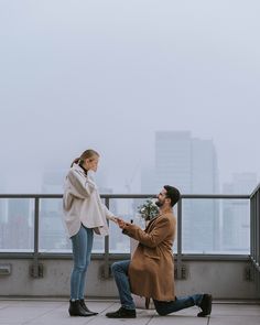 a man kneeling down next to a woman with a flower in her hand on top of a building