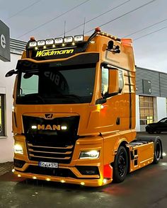 an orange semi truck parked in front of a building with lights on it's sides