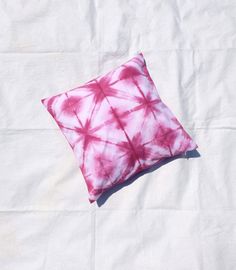 a pink and white tie - dyed pillow sitting on top of a white sheeted bed