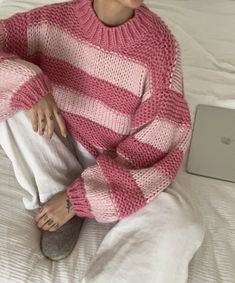 a woman sitting on top of a bed wearing a pink and white striped knit sweater