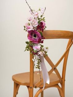 a bouquet of flowers is sitting on the back of a wooden chair with white ribbon