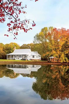 a white house sitting on top of a lake surrounded by fall foliage and trees in the background