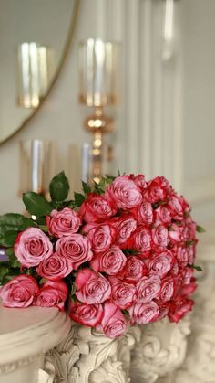 a bouquet of pink roses sitting on top of a white pedestal next to a mirror