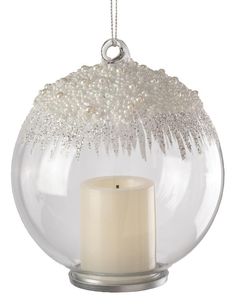 a white candle is in a glass ball ornament with snow on the inside