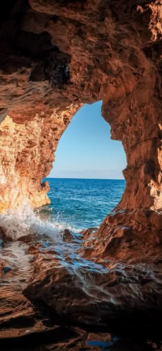 a person is standing in the middle of an ocean cave looking out at the water